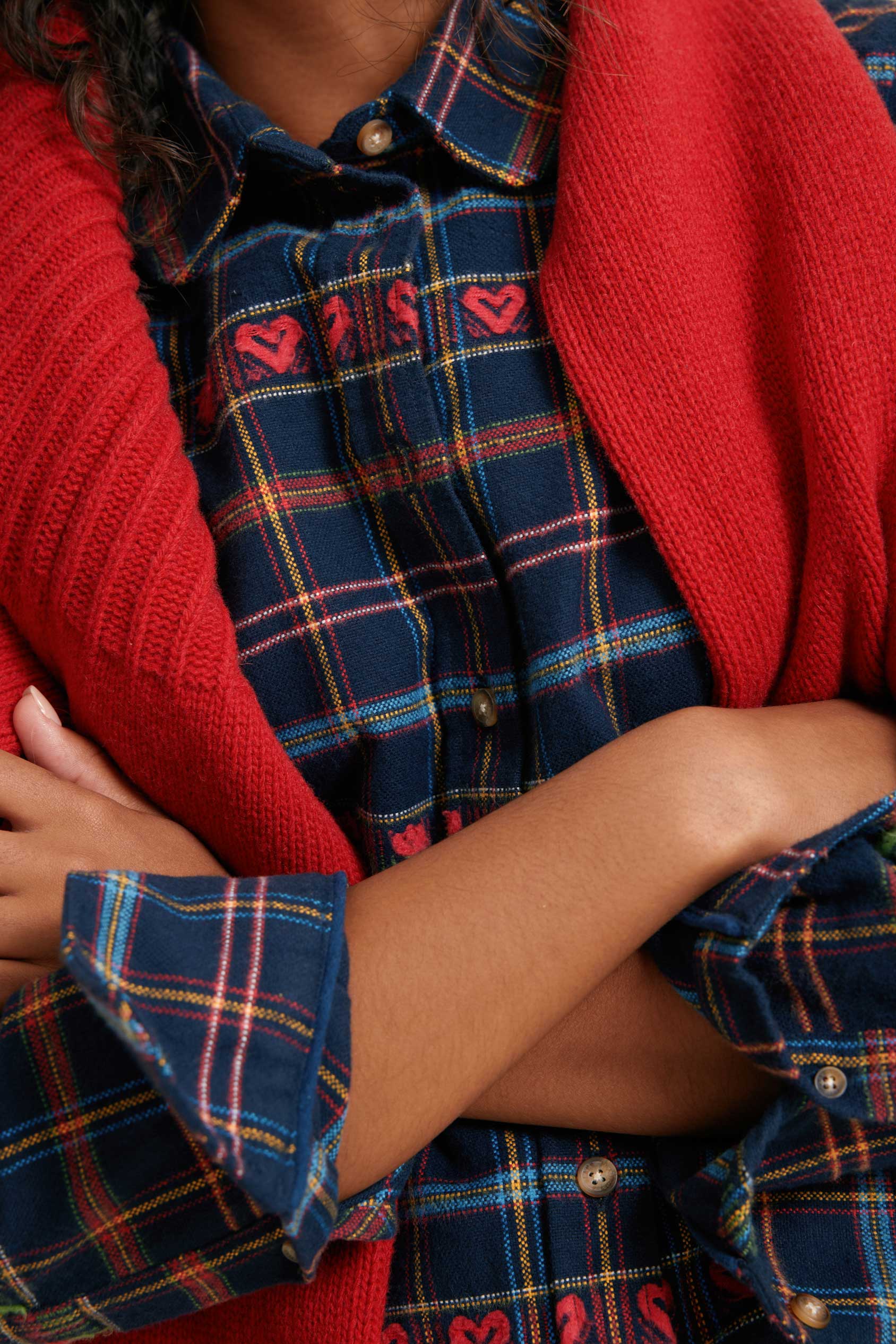 Person wearing a red cardigan over a plaid shirt with visible buttons.