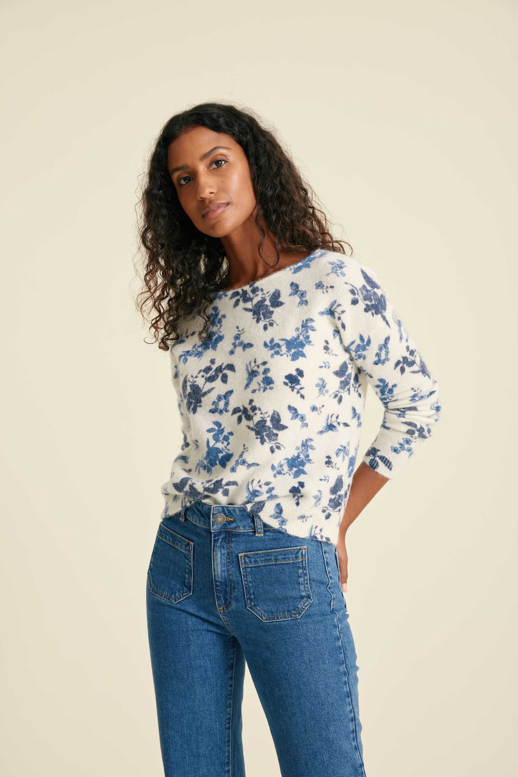 Model wearing a white blouse with blue floral pattern and blue jeans against a beige background