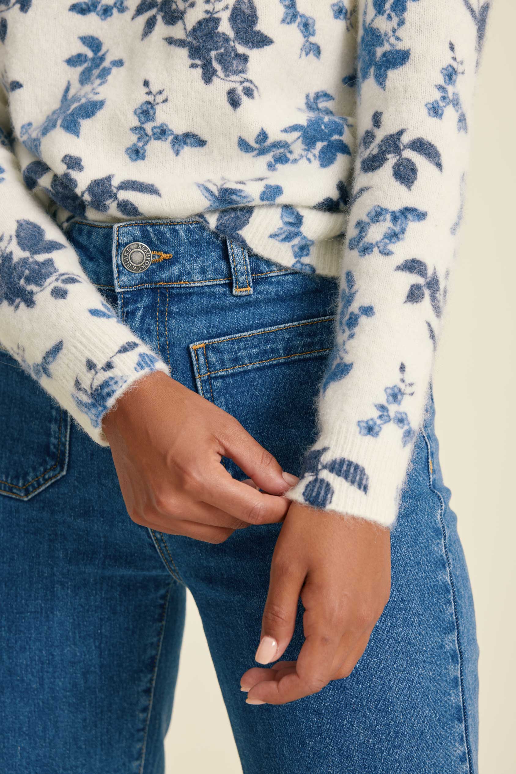 Person wearing a white sweater with blue floral pattern and blue jeans.