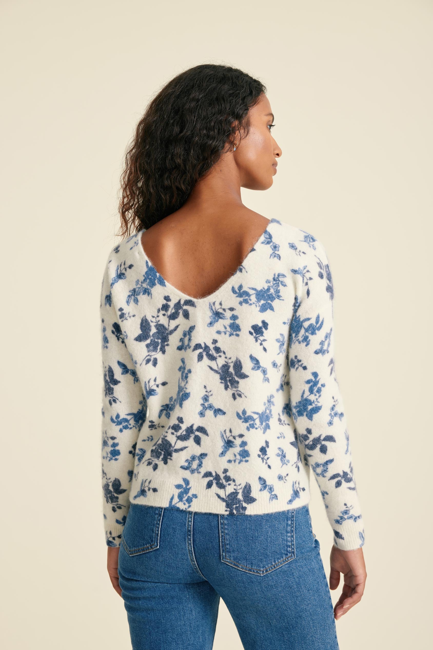 Woman wearing a floral long-sleeve top and blue jeans on a beige background