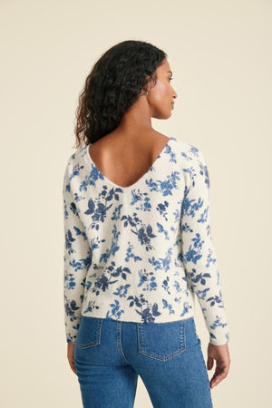 Woman wearing a floral long-sleeve top and blue jeans on a beige background