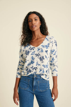 Woman wearing a floral long-sleeve top and blue jeans against a beige background