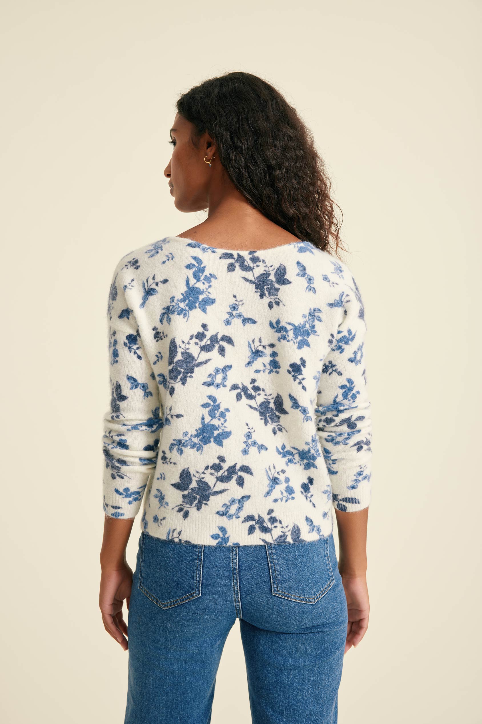 Woman wearing a floral long-sleeve top and blue jeans on a beige background