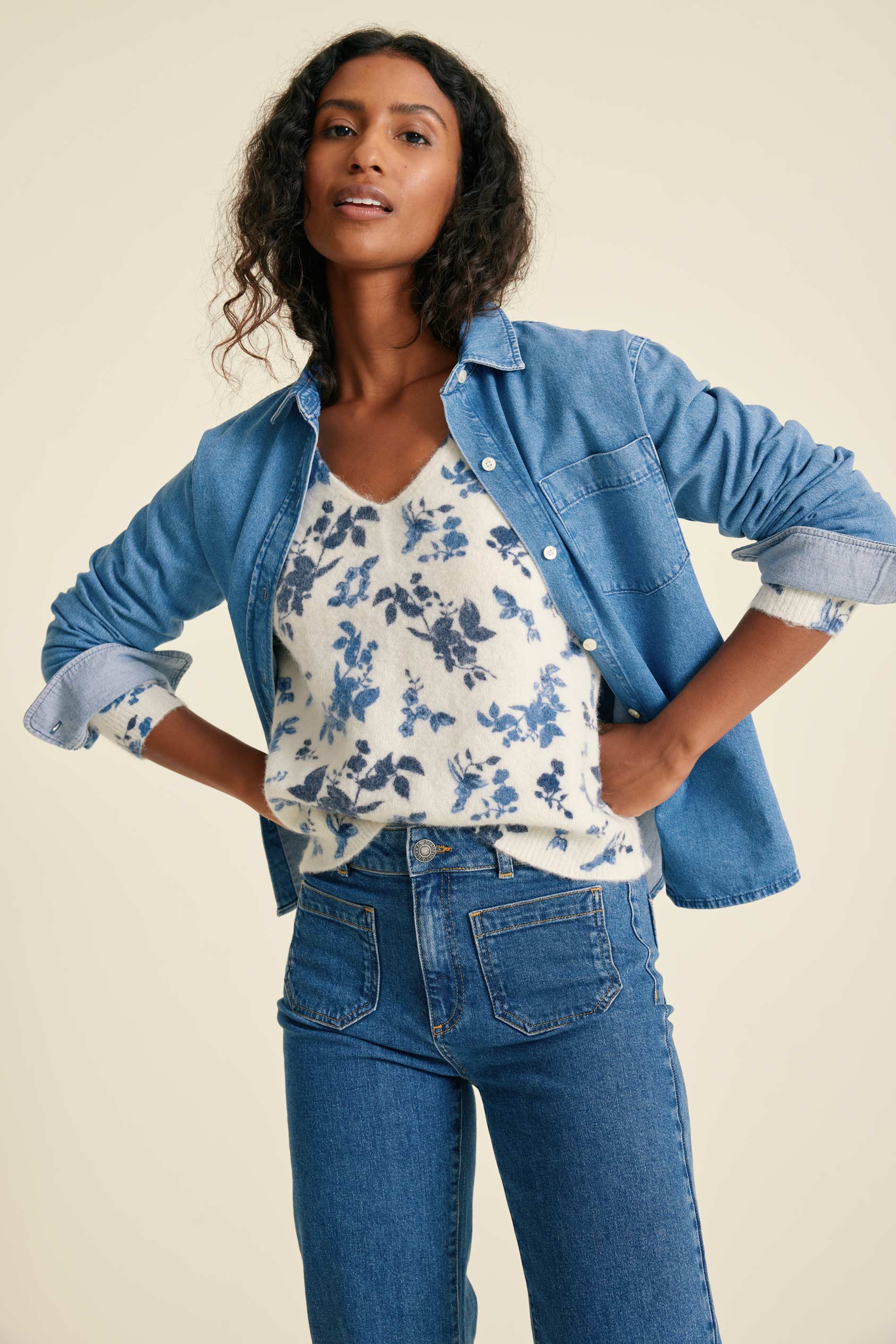 Woman wearing a denim shirts, floral top, and jeans on a beige background