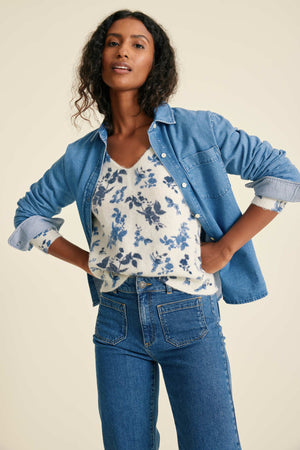 Woman wearing a denim shirts, floral top, and jeans on a beige background