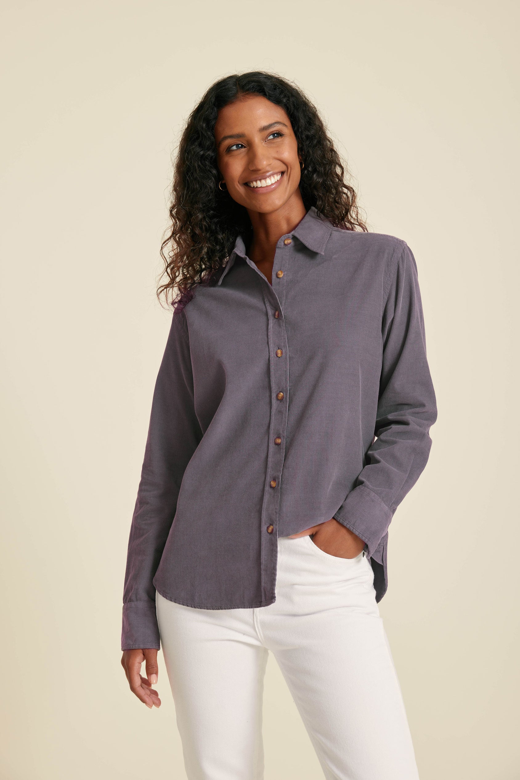 Woman wearing a purple button-up shirt and white pants against a beige background