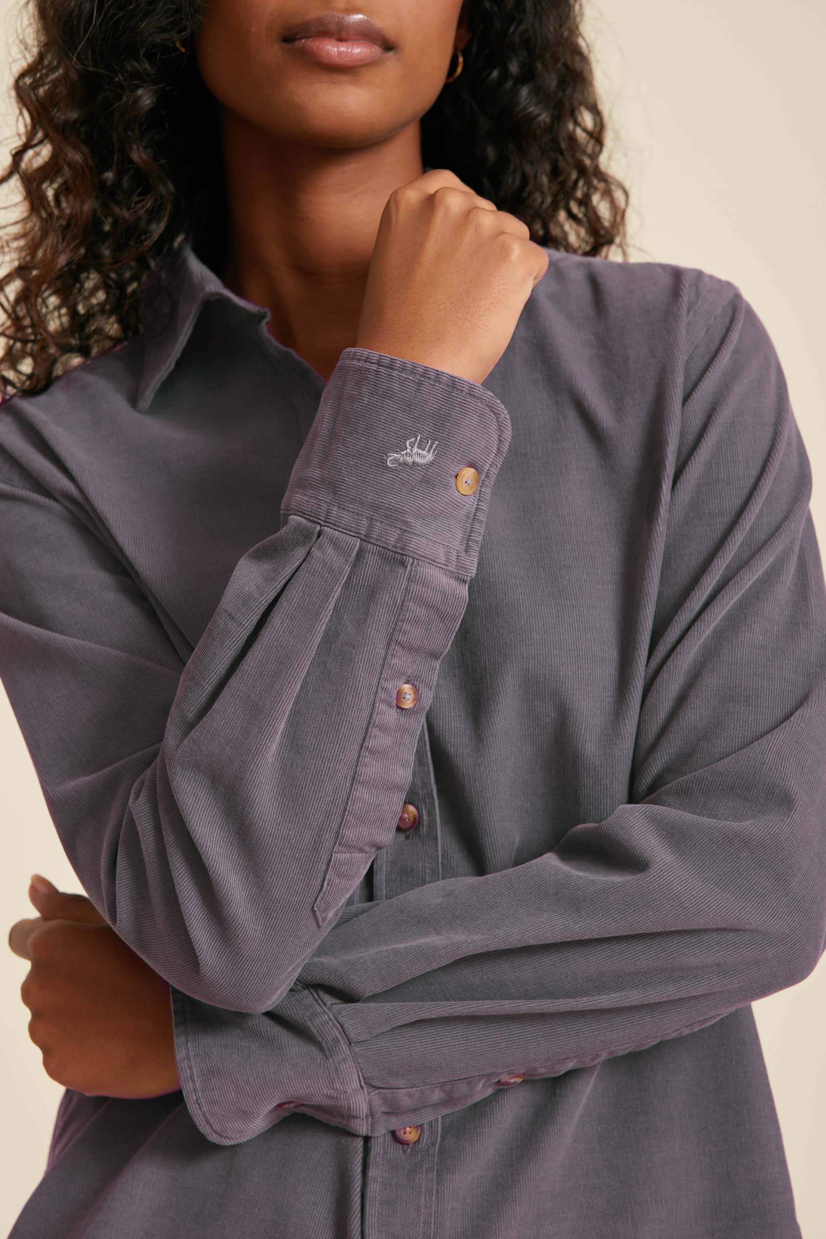 Person wearing a gray button-up shirt with a brand logo on a beige background