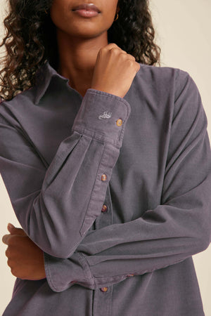Person wearing a gray button-up shirt with a brand logo on a beige background