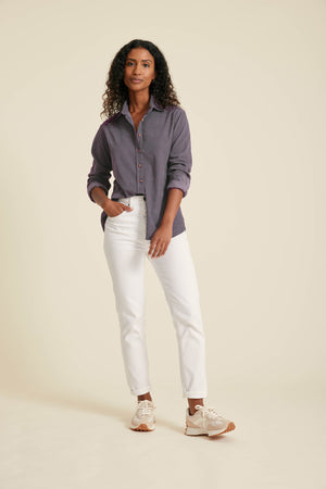 Woman wearing a purple shirt and white pants on a beige background
