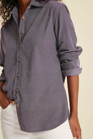 Person wearing a gray button-up shirt with rolled-up sleeves on a beige background