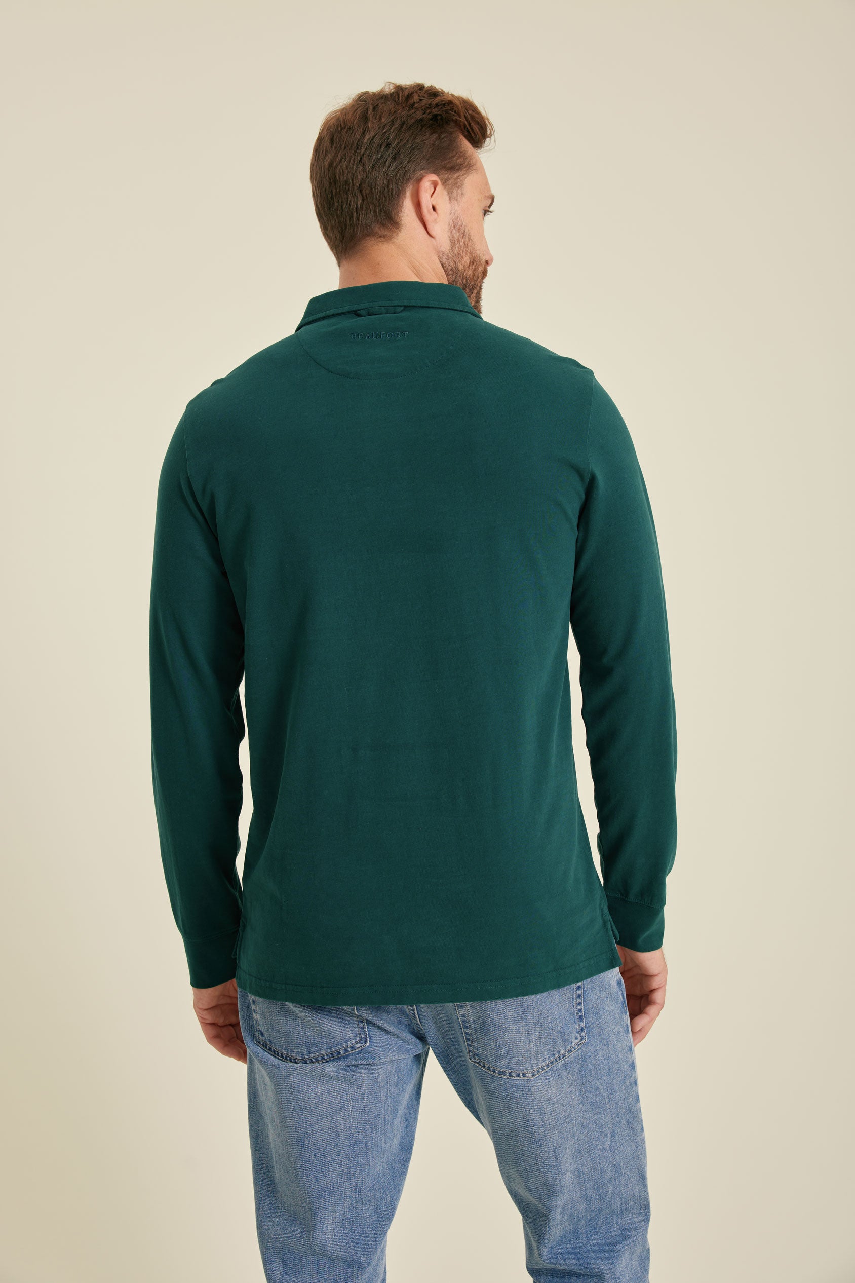 Man wearing a green long-sleeve shirt and blue jeans on a beige background