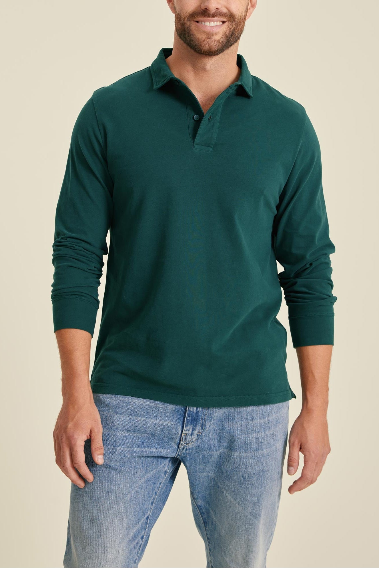 Man wearing a green long-sleeve polo shirt and blue jeans against a beige background