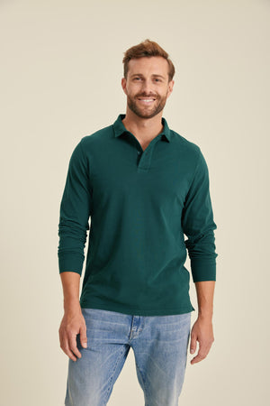 Man wearing a green long-sleeve polo shirt and blue jeans against a beige background