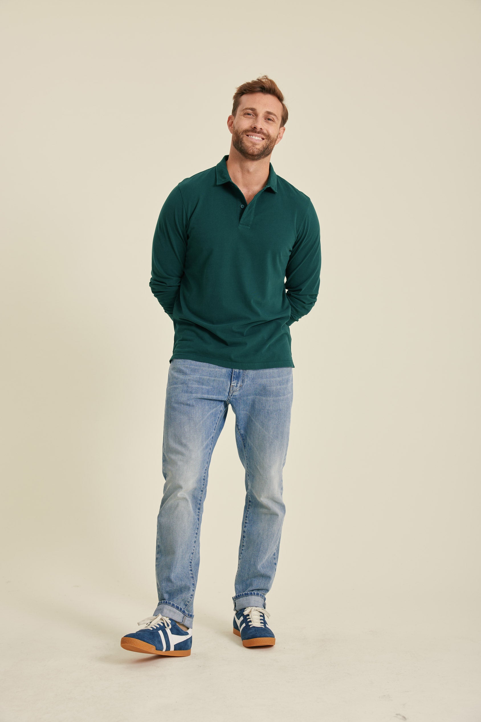 Man wearing a green sweater and blue jeans standing against a beige background