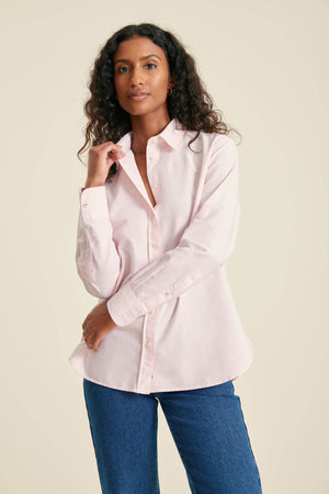 Woman wearing a light pink shirt and blue jeans against a beige background