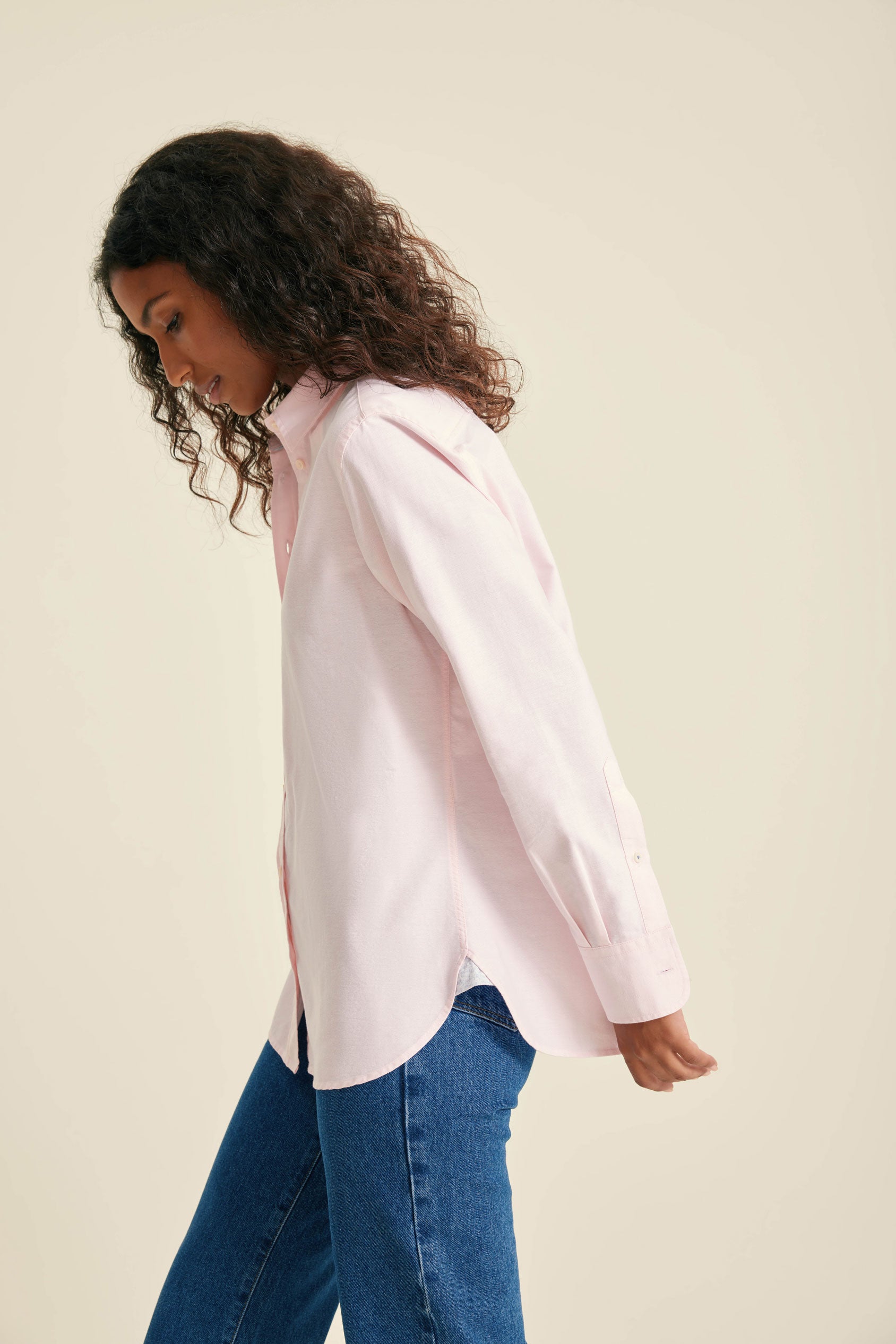 Woman wearing a light pink blouse and blue jeans against a beige background