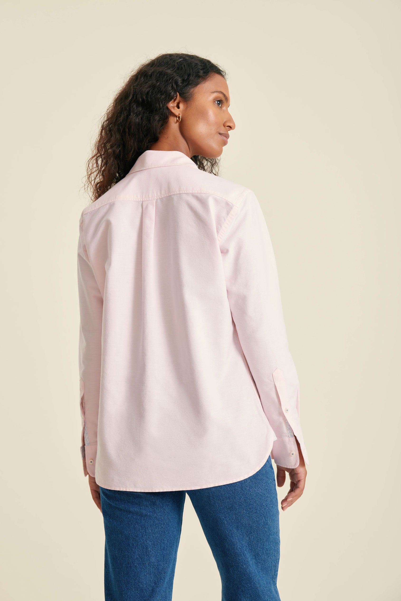 Woman wearing a light pink shirt and blue jeans against a beige background