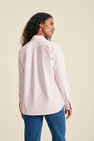 Woman wearing a light pink shirt and blue jeans against a beige background