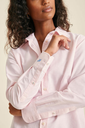 Woman wearing a light pink shirt with a brand logo on a beige background