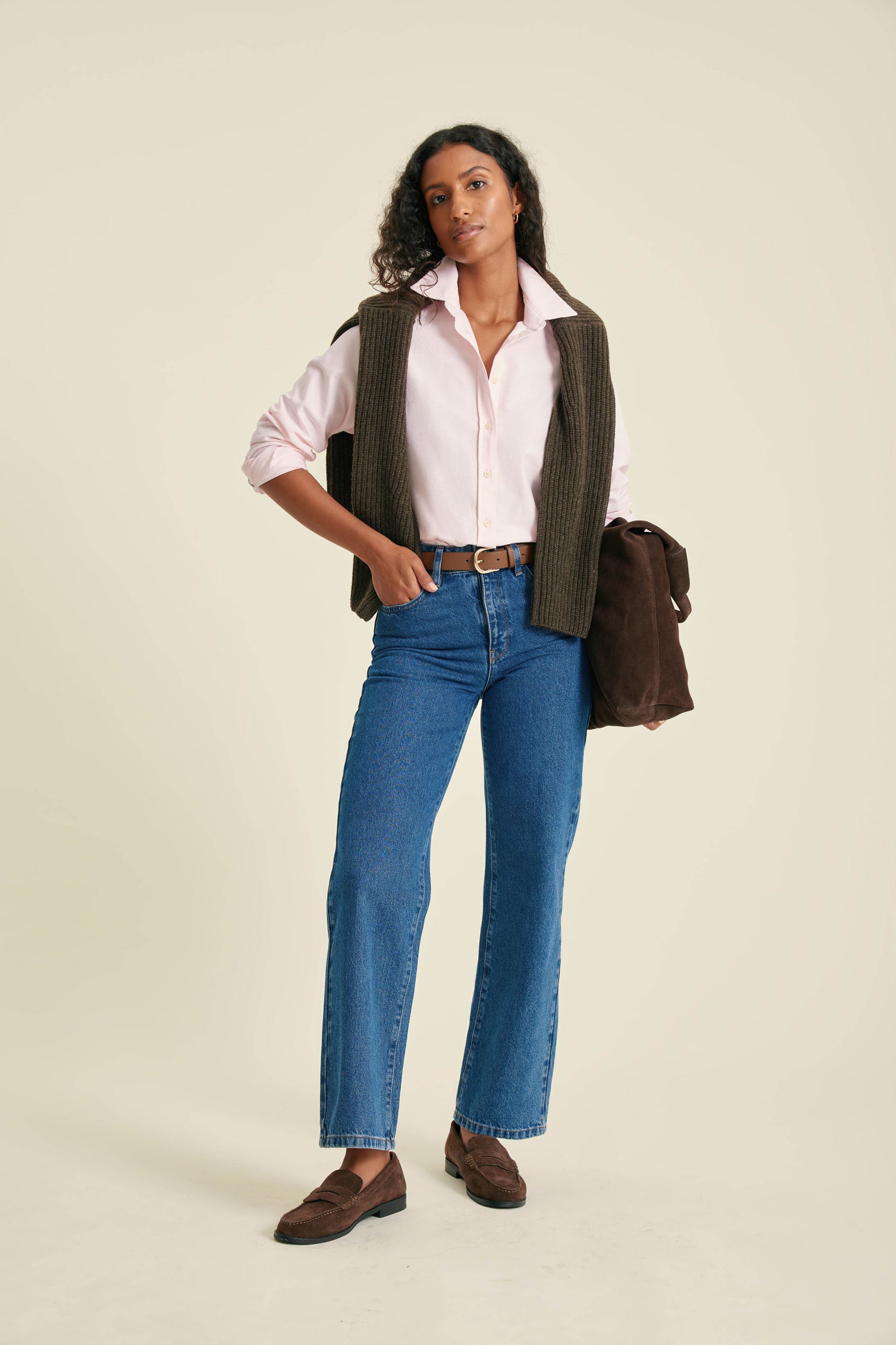 Woman wearing a vest, shirt, jeans, and shoes on a beige background