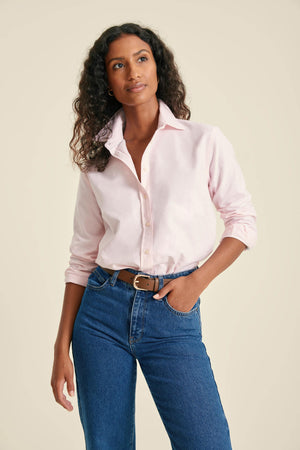 Woman wearing a light pink shirt and blue jeans against a beige background