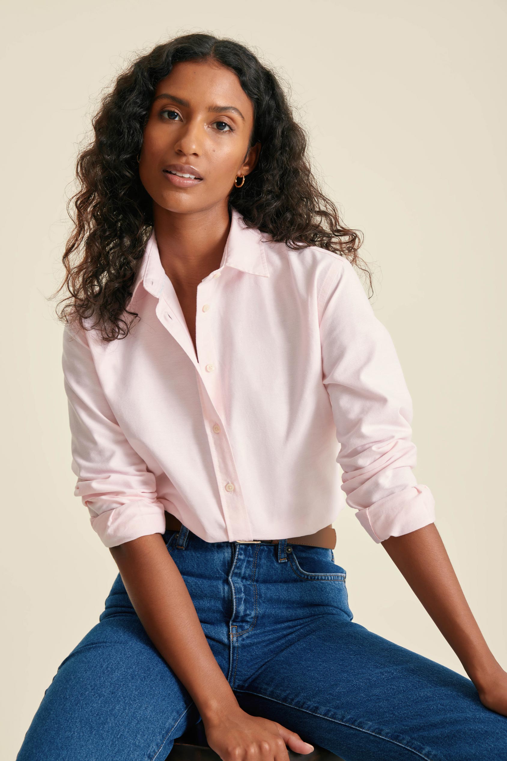 Woman wearing a light pink shirt and blue jeans against a beige background
