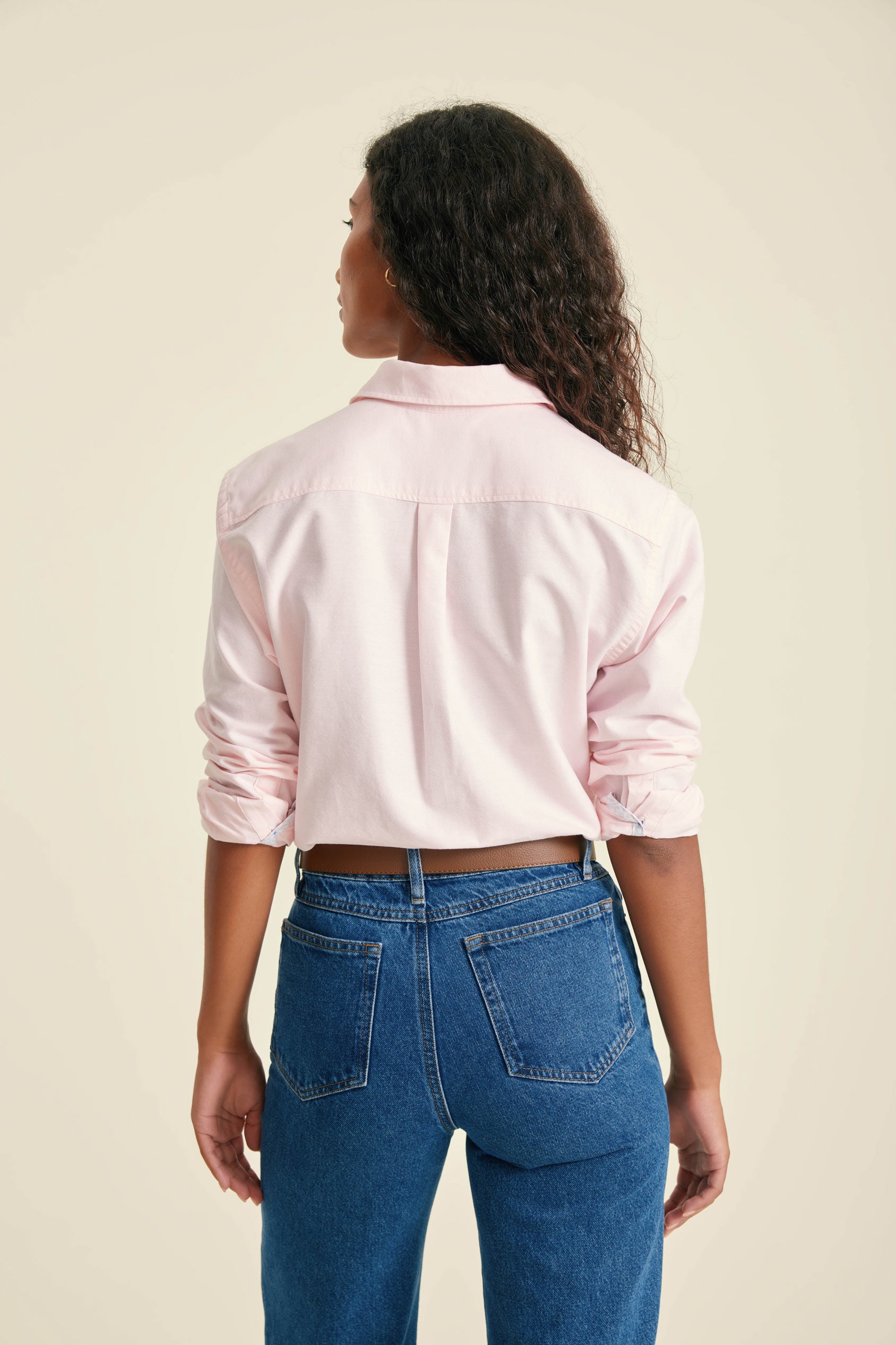 Person wearing a light pink shirt and blue jeans on a beige background