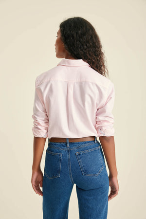 Person wearing a light pink shirt and blue jeans on a beige background