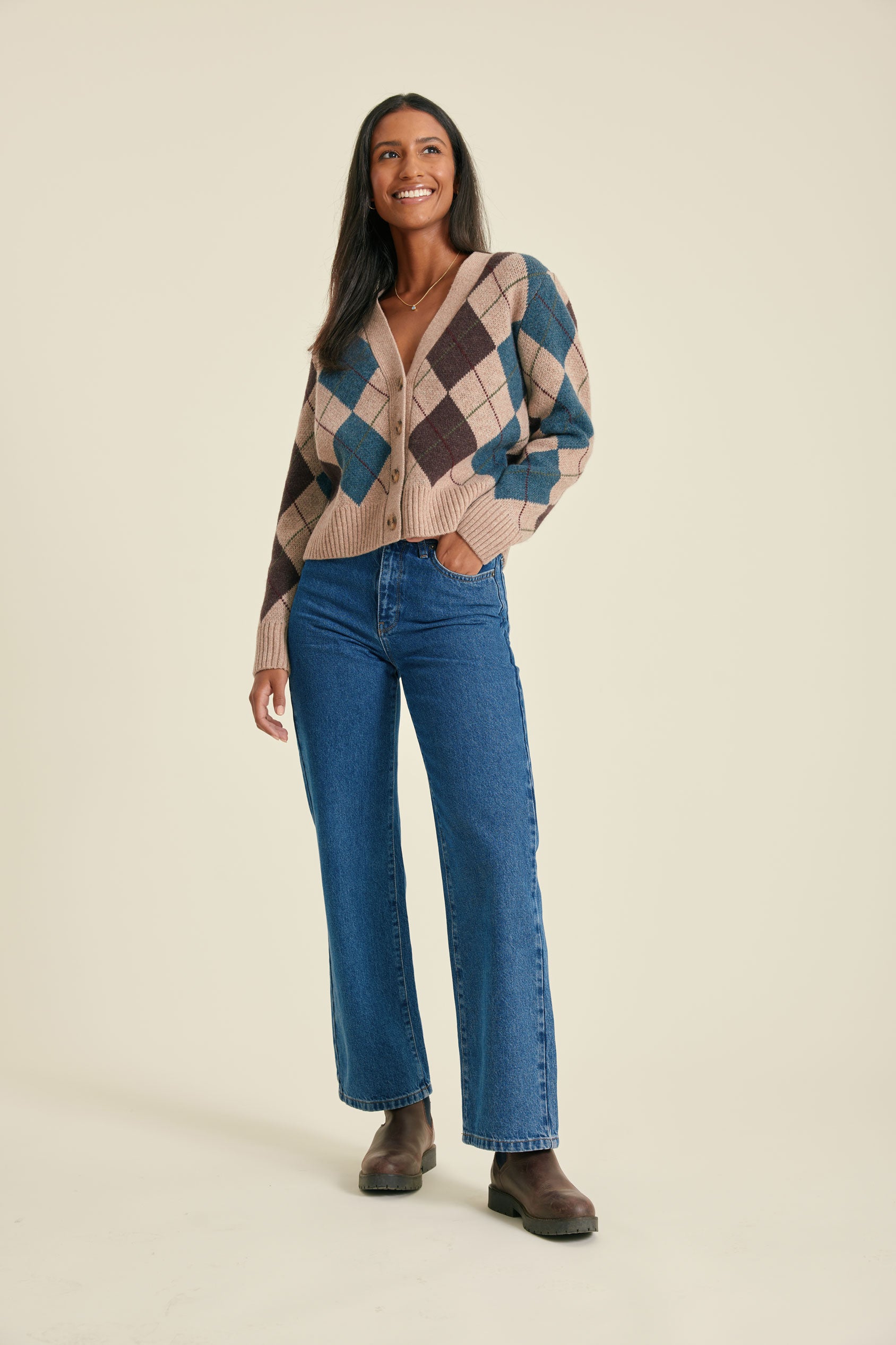 Woman wearing a patterned cardigan and blue jeans on a beige background