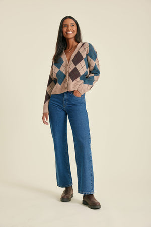 Woman wearing a patterned cardigan and blue jeans on a beige background