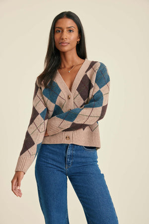 Woman wearing a patterned cardigan and blue jeans on a beige background