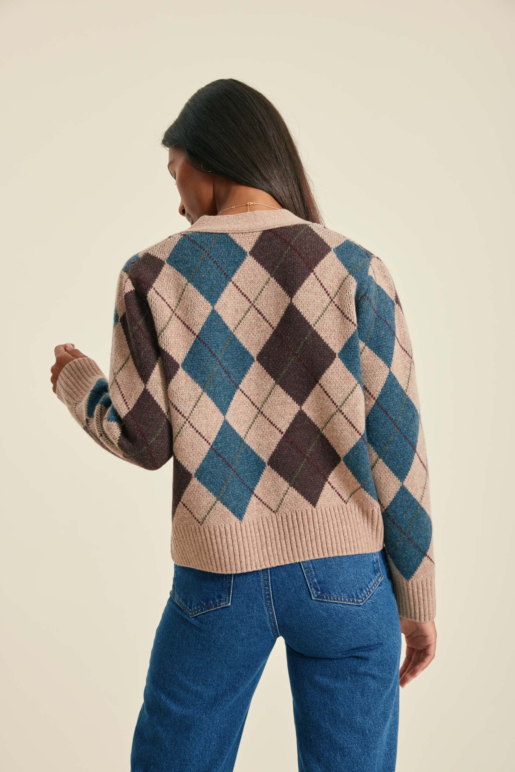 Person wearing a patterned sweater and blue jeans on a beige background