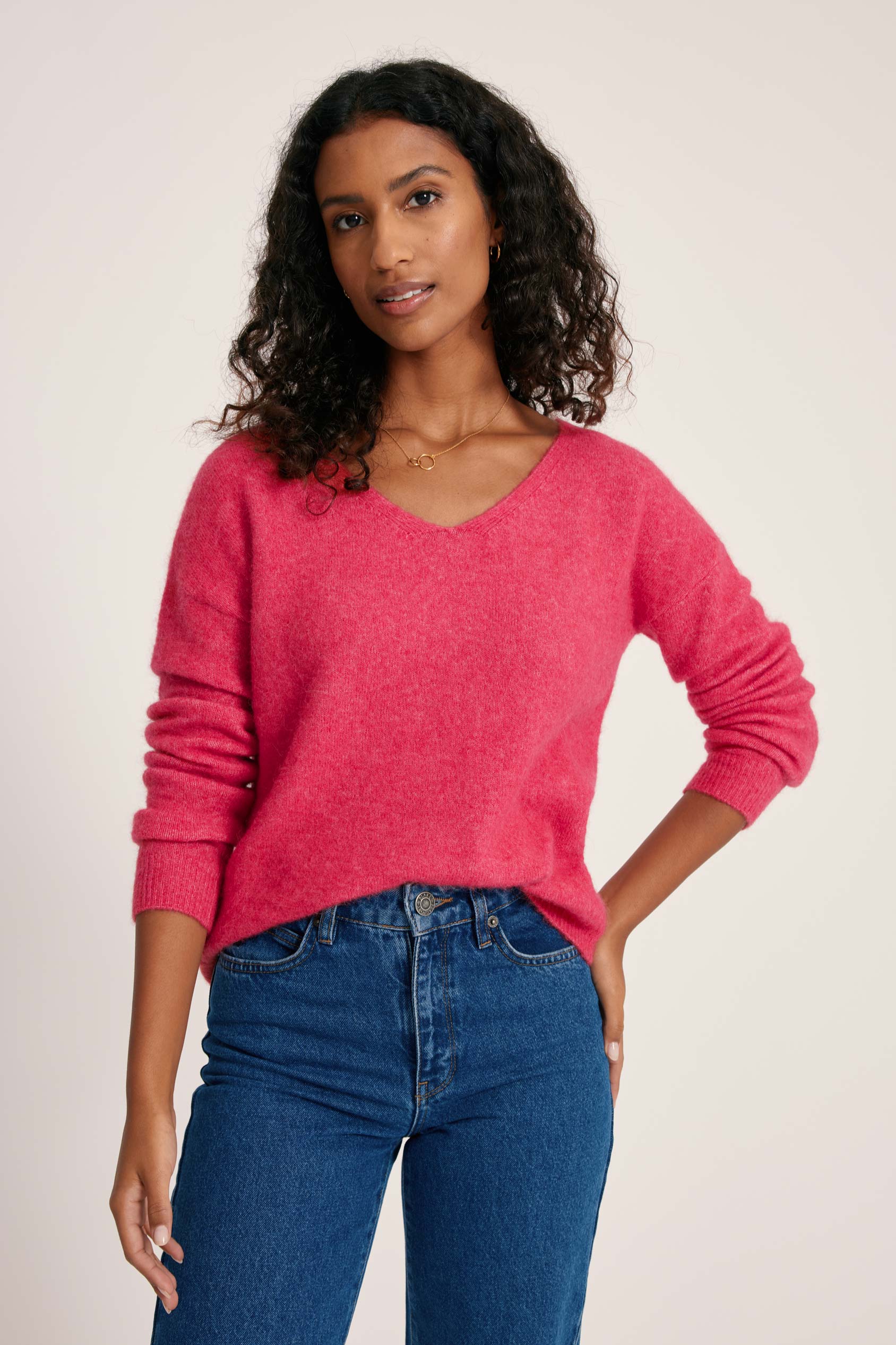 Woman wearing a pink sweater and blue jeans on a plain background