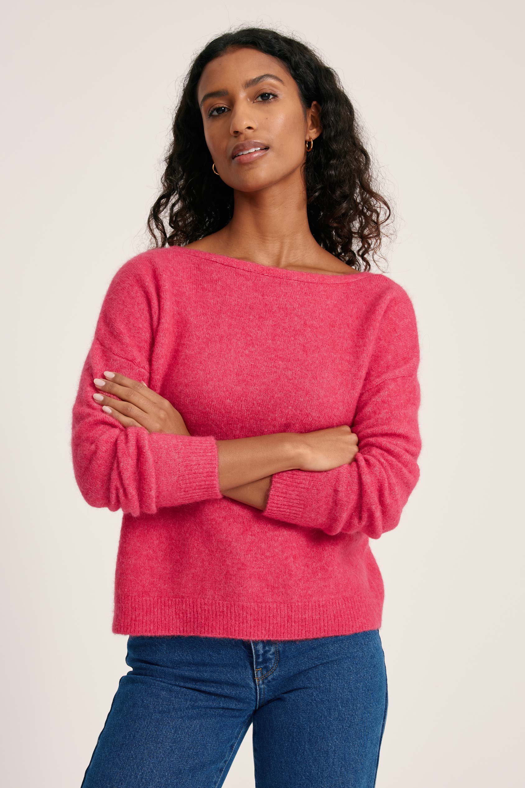Woman wearing a pink sweater and blue jeans against a plain background