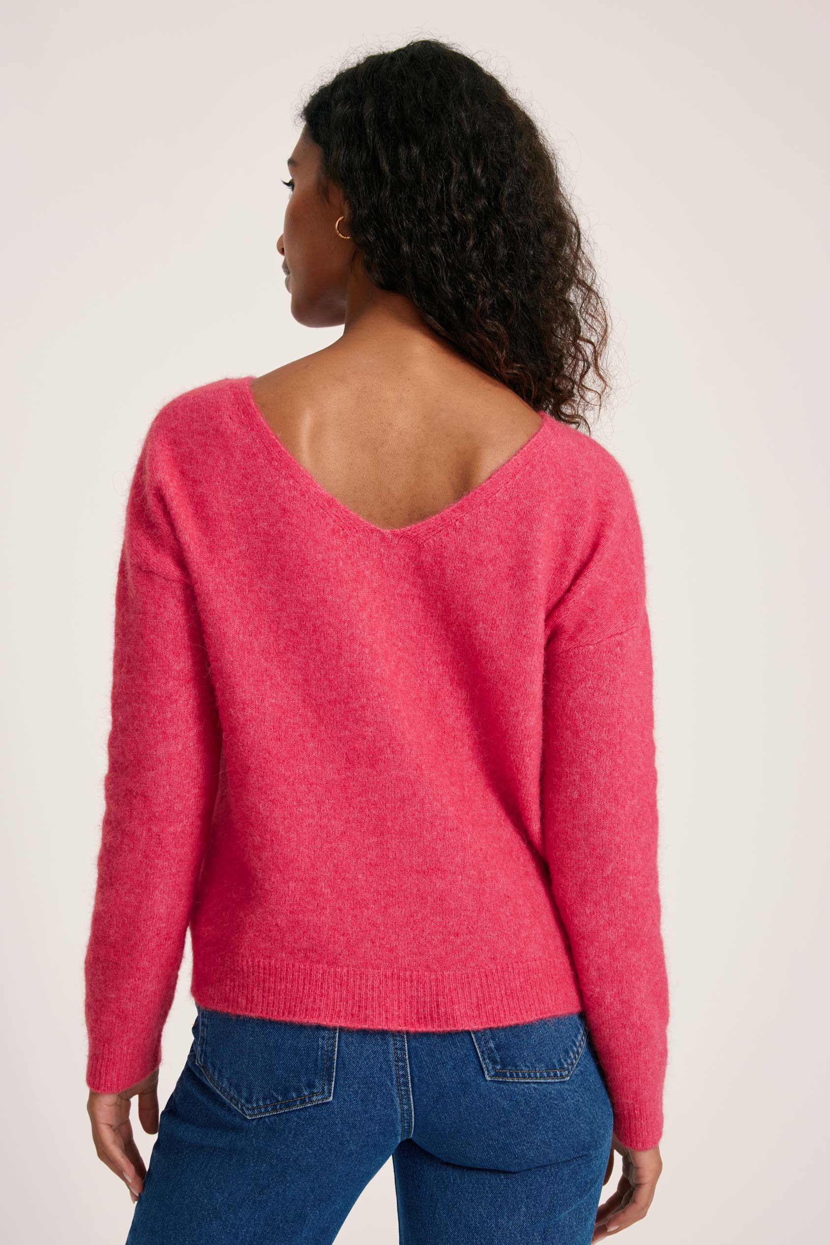 Person wearing a pink sweater and blue jeans on a plain background