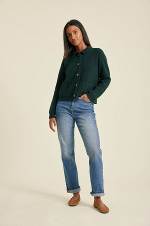 Woman wearing a dark green shirt and blue jeans on a beige background