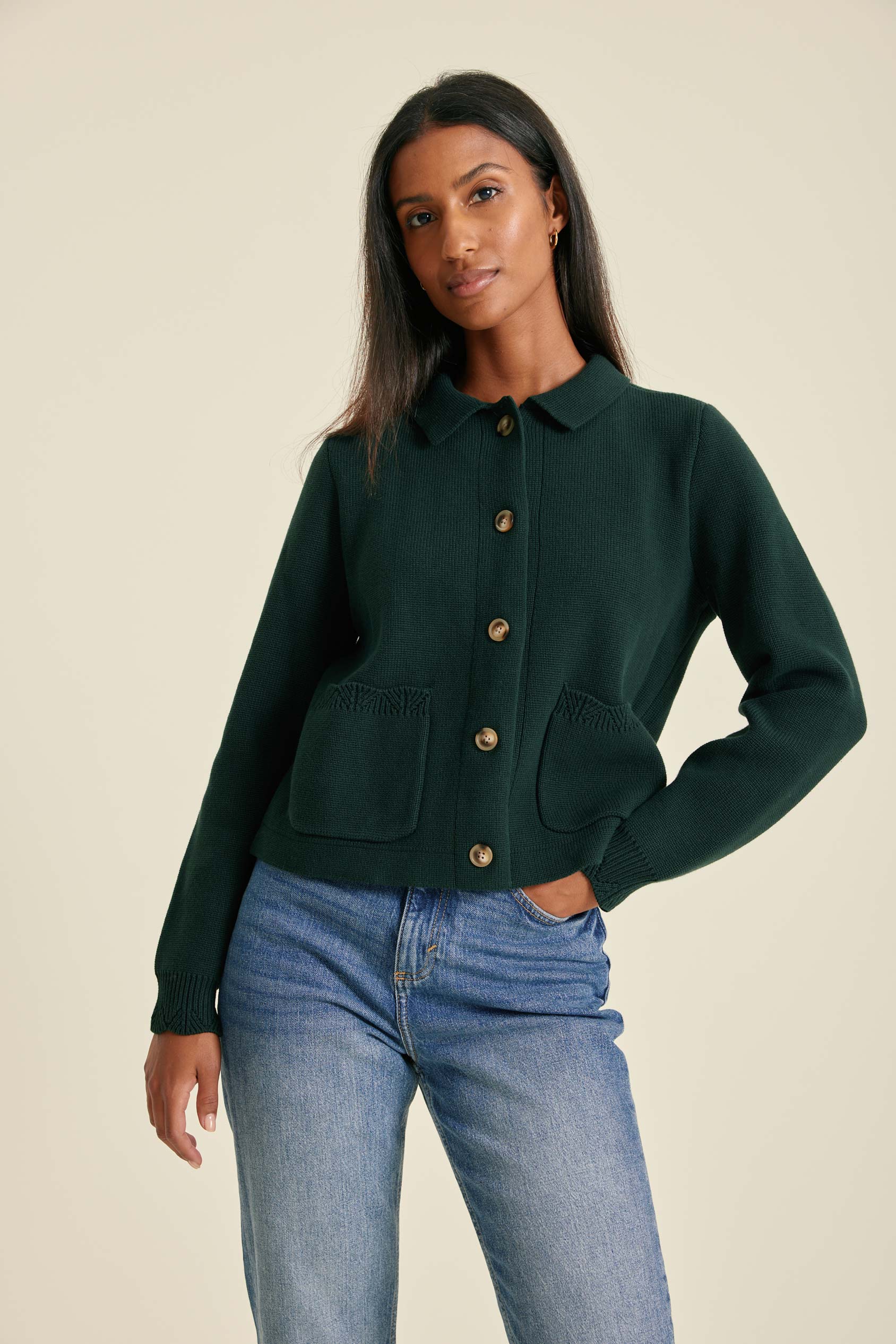 Woman wearing a dark green jacket with gold buttons on a beige background