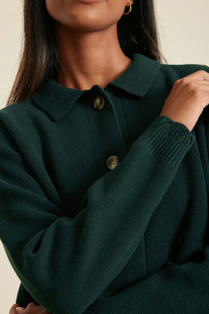 Person wearing a dark green sweater with a neutral background