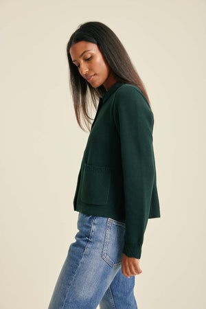 Woman wearing a dark green sweater and blue jeans on a beige background