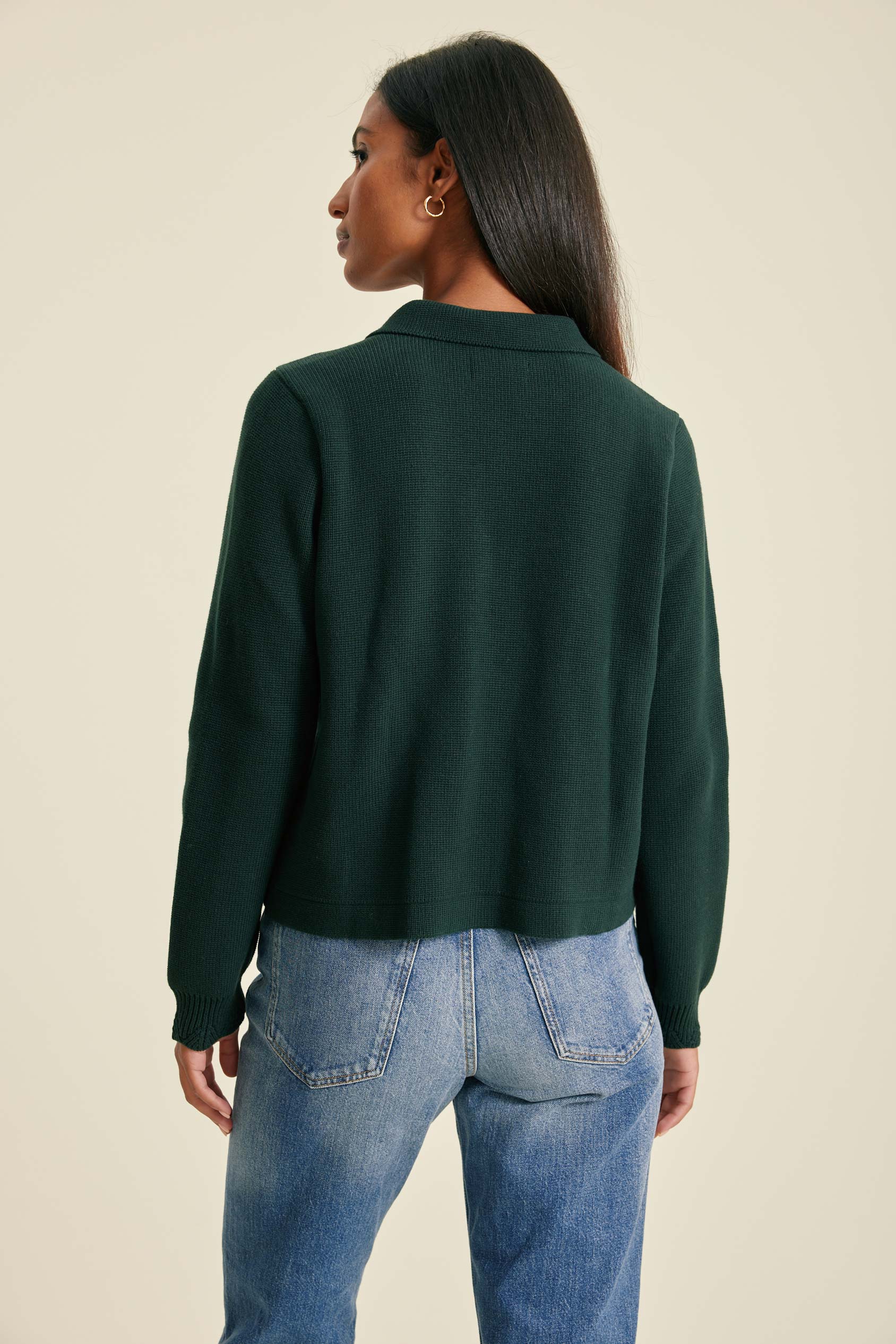 Person wearing a green sweater and blue jeans on a beige background