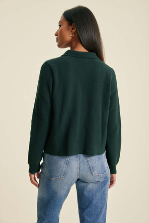 Person wearing a green sweater and blue jeans on a beige background