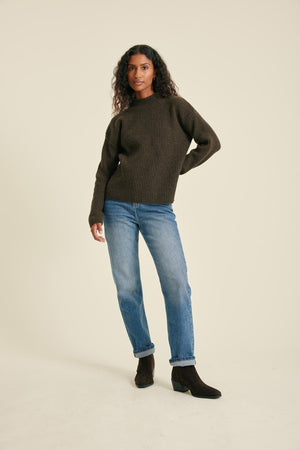 Woman wearing a dark green sweater and blue jeans on a beige background
