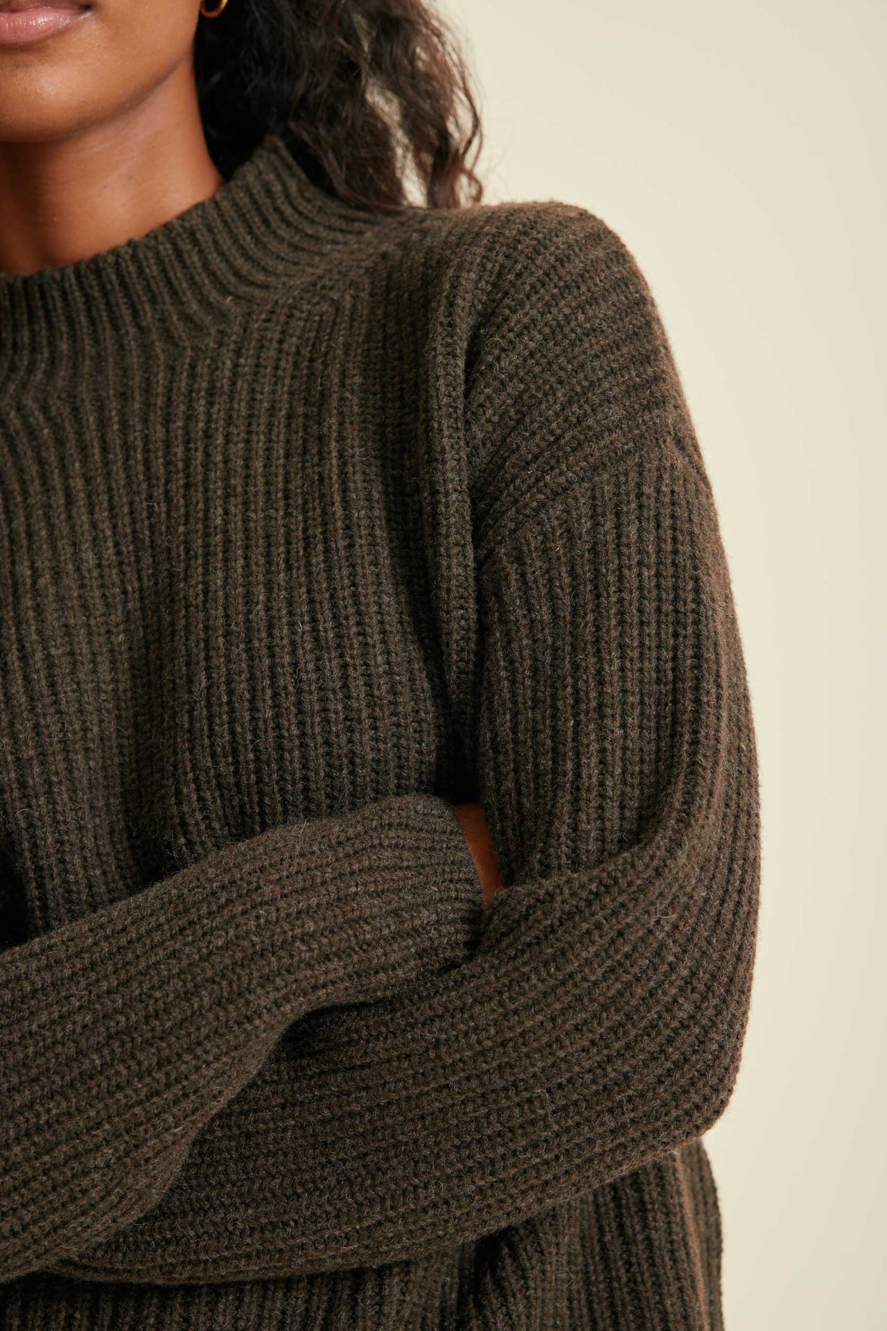 Close-up of a person wearing a brown ribbed sweater against a neutral background