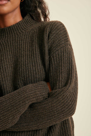 Close-up of a person wearing a brown ribbed sweater against a neutral background
