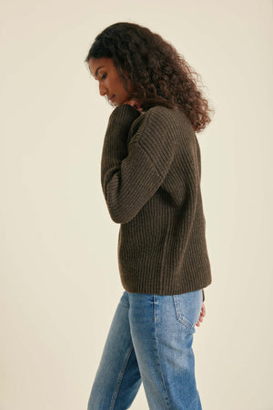Woman wearing a brown sweater and blue jeans against a beige background