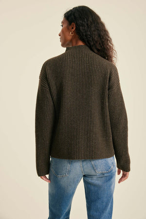 Person wearing a brown ribbed sweater and blue jeans on a beige background