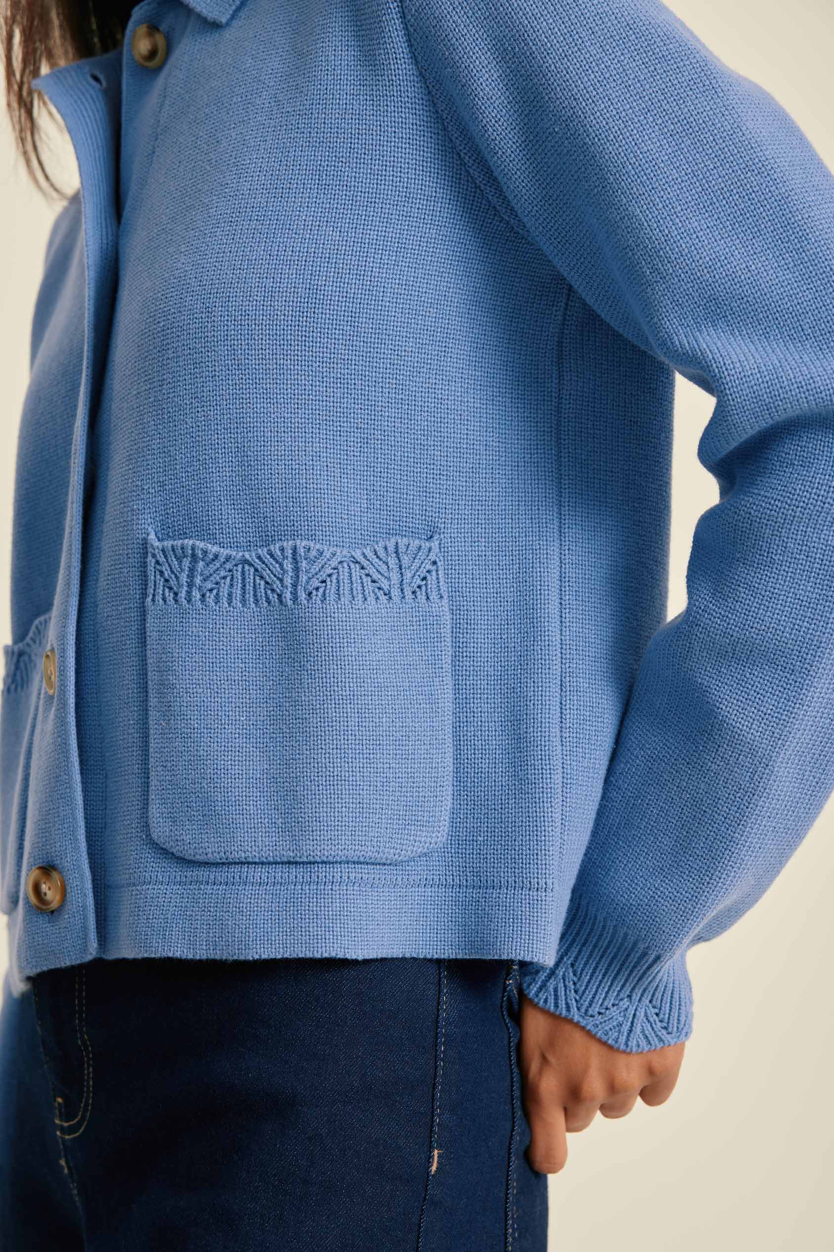 Blue knitted jacket with a textured pocket on a neutral background
