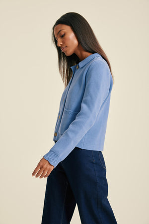 Woman wearing a blue denim jacket and dark pants on a beige background