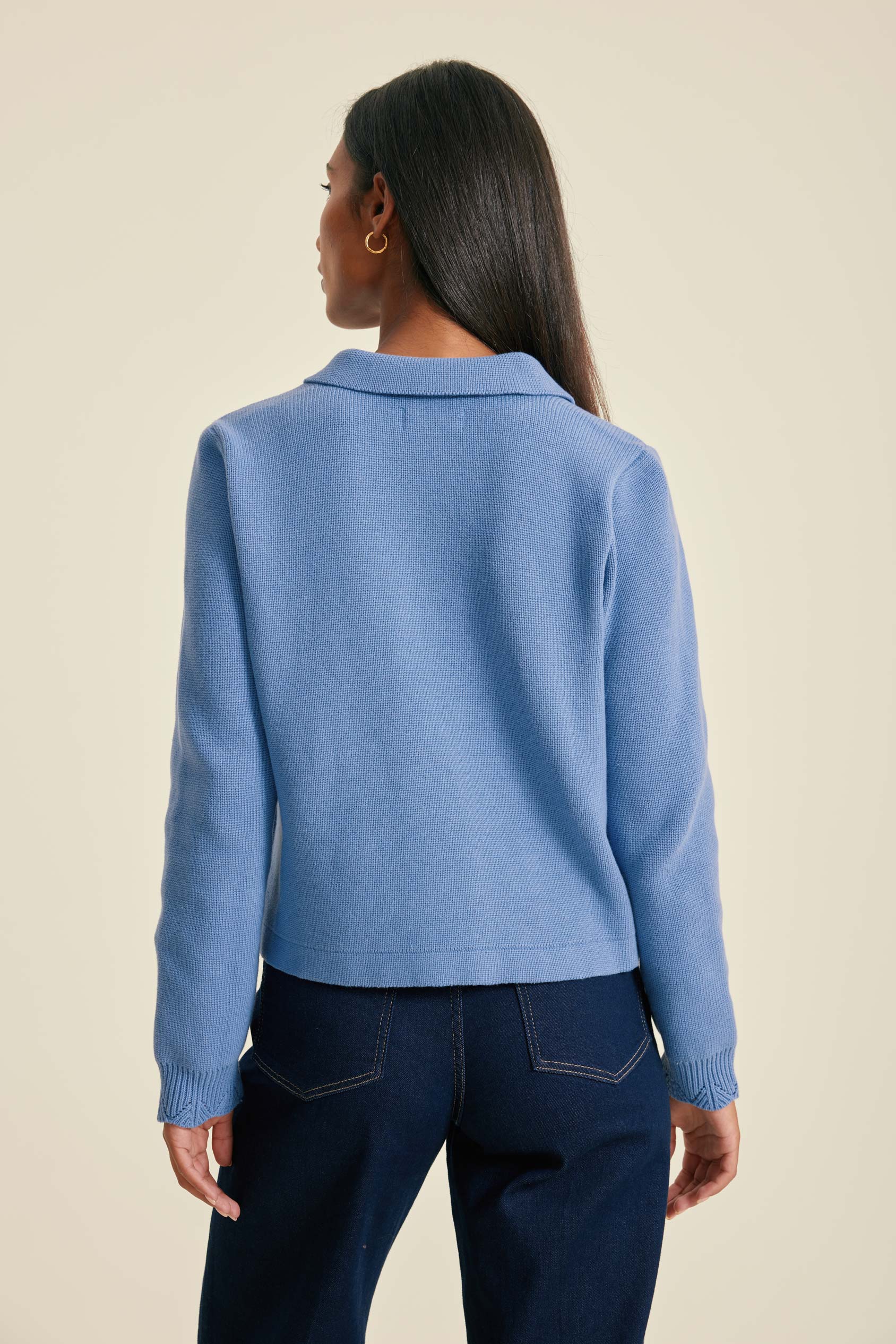 Person wearing a light blue sweater and dark blue jeans on a beige background