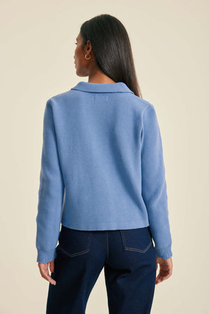 Person wearing a light blue sweater and dark blue jeans on a beige background